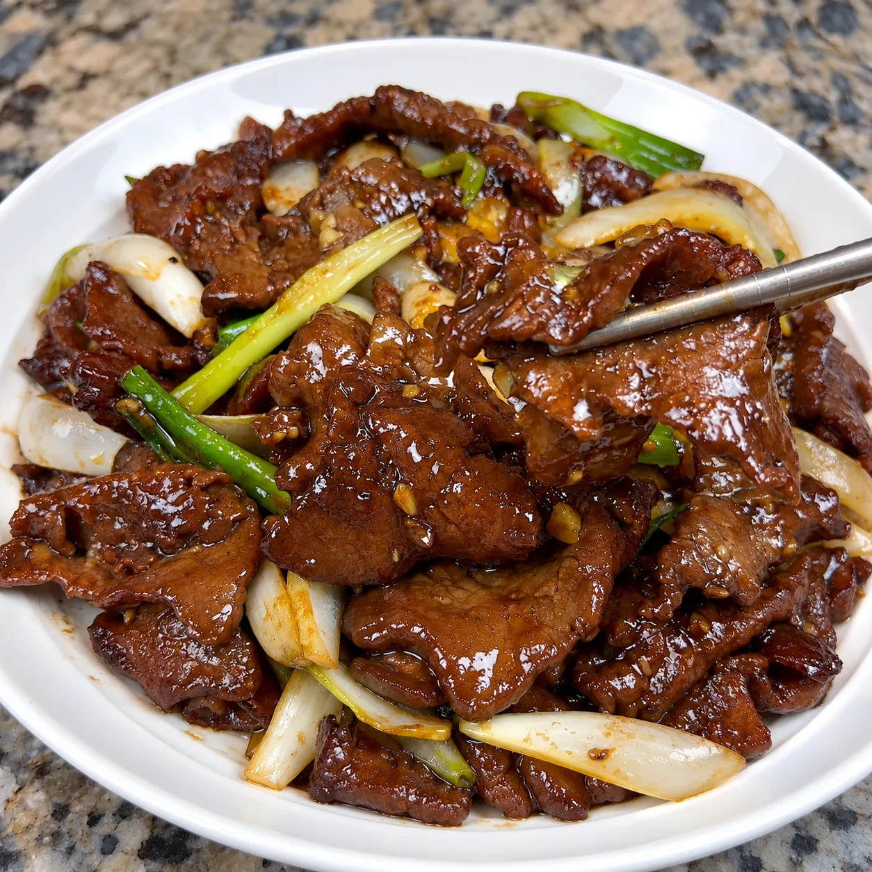Bowl of Chinese-style beef and onion stir fry with green onion over rice
