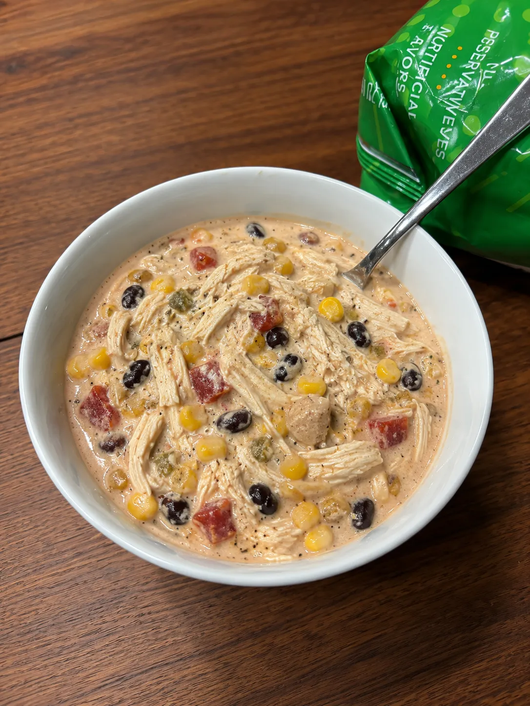 Creamy chicken taco soup with black beans, corn, and tomatoes in a white bowl