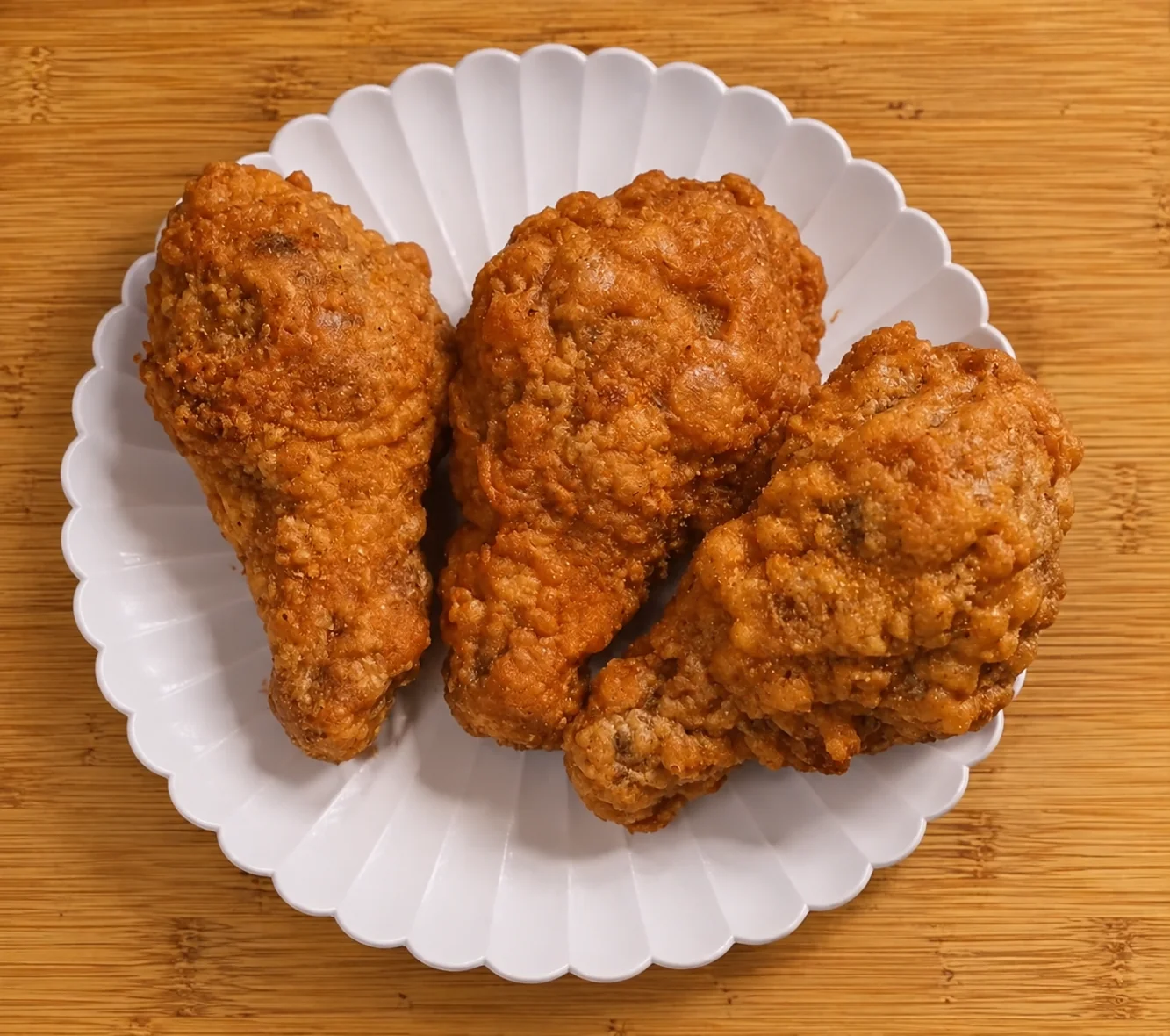 Three extra crispy buttermilk fried chicken drumsticks on a white plate
