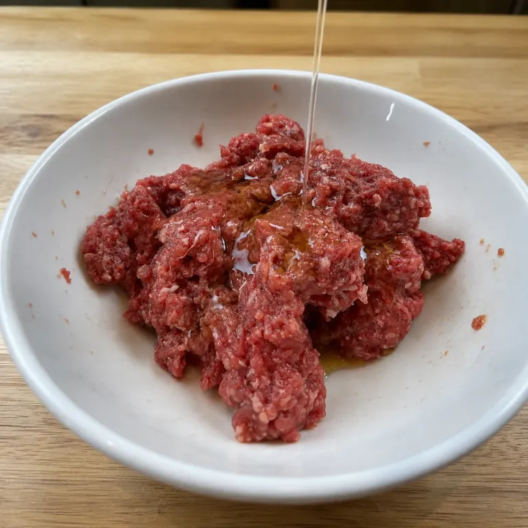 Marinade being poured over raw ground beef in a white bowl