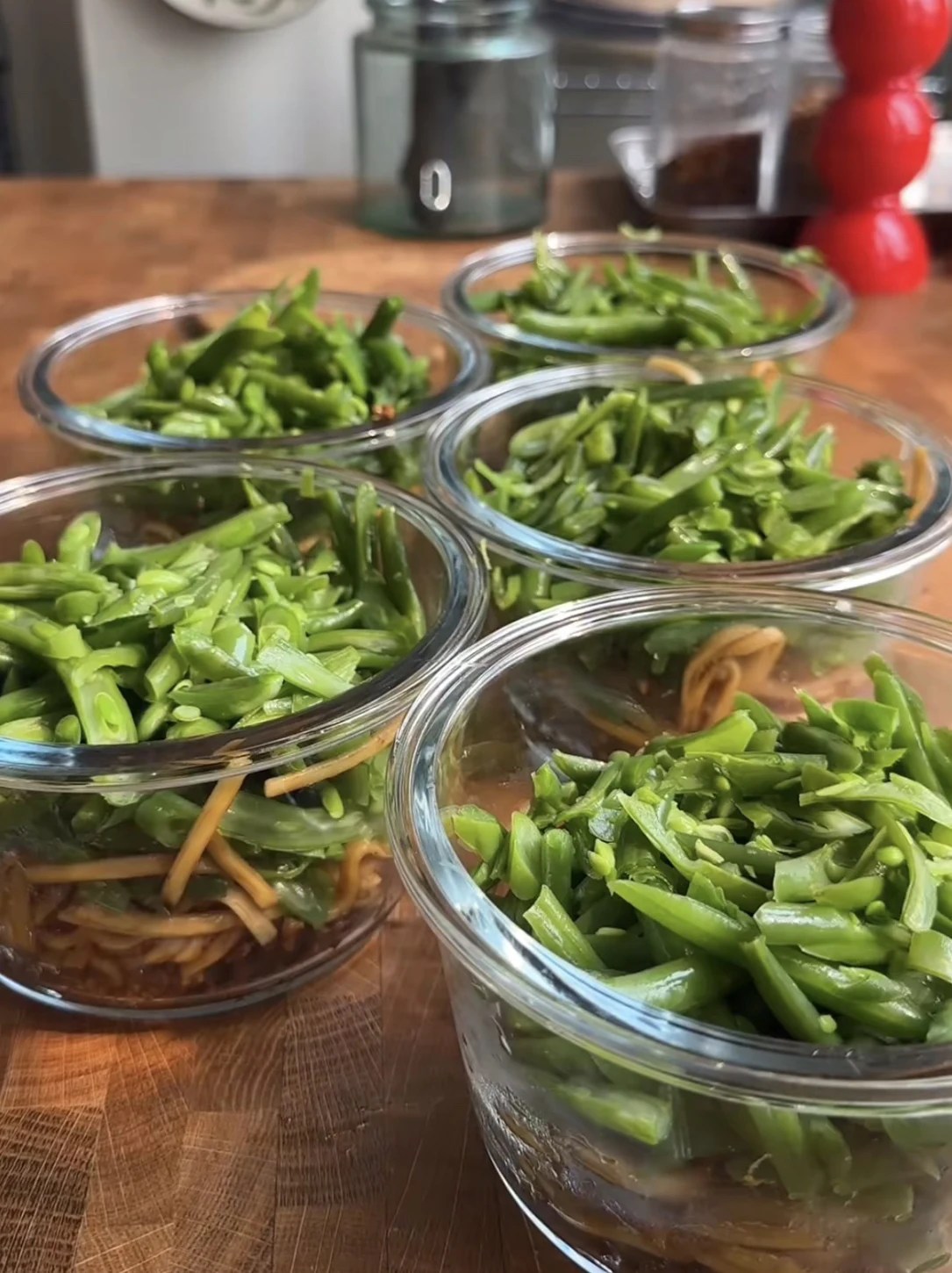 Five glass containers of honey garlic chicken noodle bowls with green beans