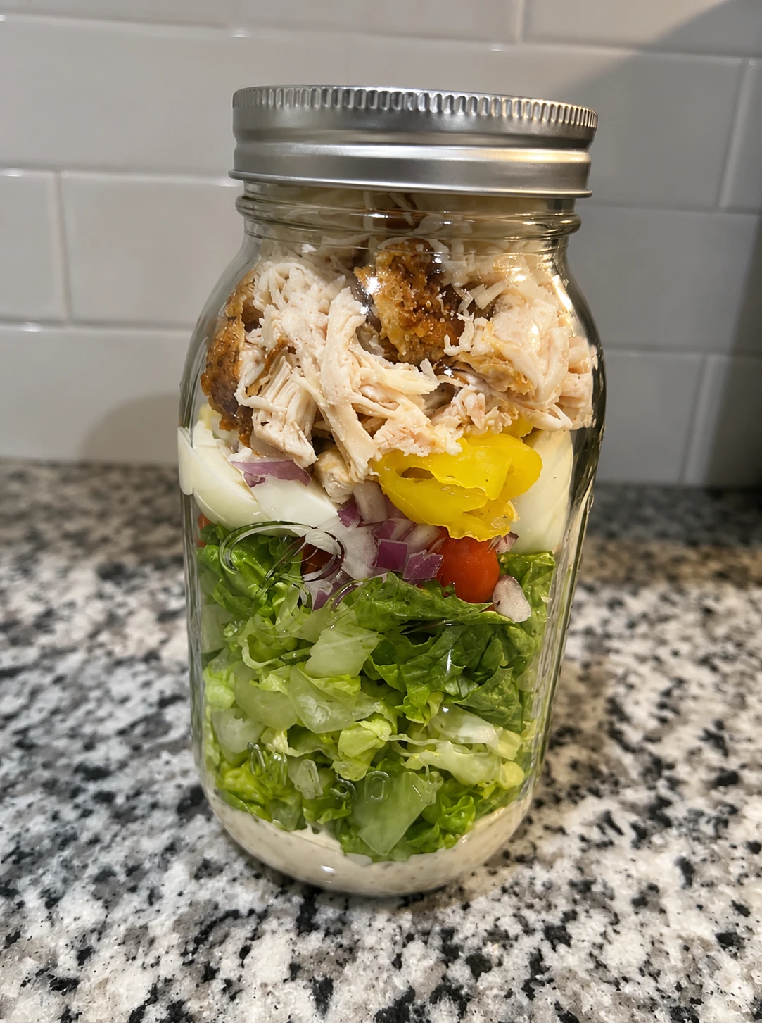Layered mason jar salad with greens, veggies, eggs, and chicken